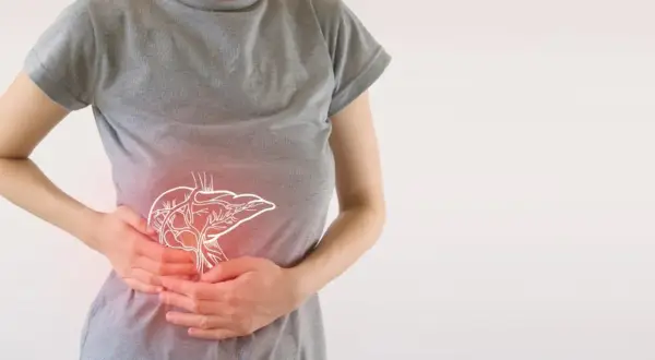Osoba trzymająca się za brzuch, gdzie widoczny jest zarys wątroby. Może to symbolizować problemy trawienne lub skutki uboczne enzymów trawiennych.