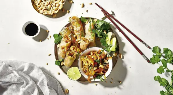 Frühlingsrollen mit Erdnüssen, Limette und Koriander – ein typisch asiatisches Essen, serviert mit Sojasauce und Stäbchen.