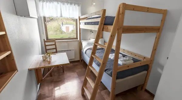 Enkel och mysig rum på vandrarhem Åre med våningssäng, litet bord och fönster med utsikt över grönskande landskap.