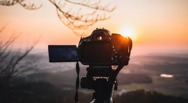 Aparat fotograficzny na statywie na tle zachodzącego słońca.