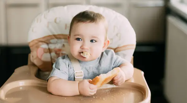 Słodki maluch w krzesełku z chlebkiem w rączce. Zastanawiasz się, jaki chleb dla rocznego dziecka będzie najlepszy? Ten wygląda apetycznie!