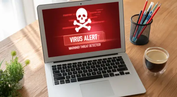 Laptop z czerwonym ekranem i ostrzeżeniem "VIRUS ALERT". To pokazuje, co robi trojan: infekuje system i wyświetla alarm.