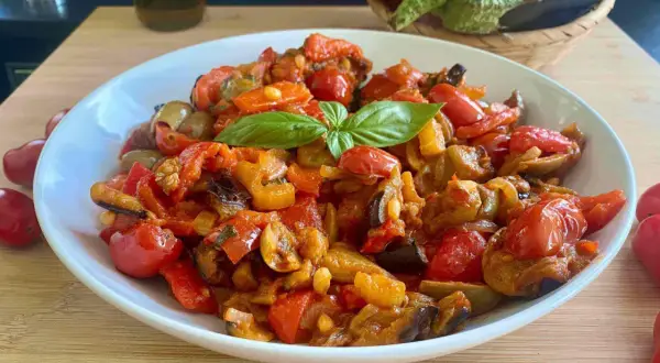 Caponata ricetta semplice: melanzane, peperoni e pomodorini cotti insieme, guarnita con basilico fresco. Un contorno saporito e colorato.