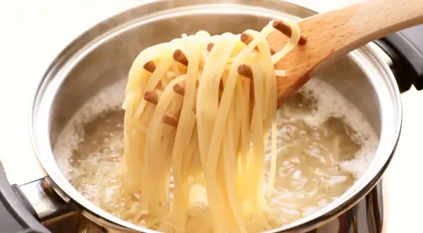 Spaghetti fraîchement cuits à l'italienne, retirés d'une casserole d'eau bouillante avec une cuillère en bois.