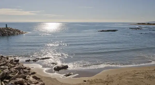 Costa de Villaricos con un faro en un rompeolas de rocas. El sol brilla sobre el mar azul y la arena dorada.