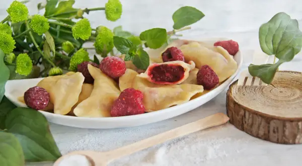 Pyszne pierogi z malinami, ozdobione świeżymi malinami i zielonymi listkami. Idealne na letni deser.