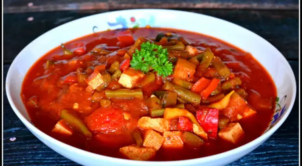 Pyszne leczo z tofu, z fasolką szparagową i papryką w sosie pomidorowym, udekorowane natką pietruszki.
