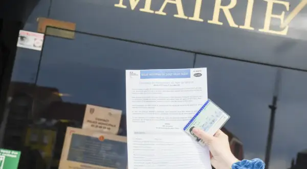 Main dans la main, une carte d'identité française et un formulaire de demande de changement de nom de famille sont présentés devant la mairie. Un geste pour de fautereau vassel.