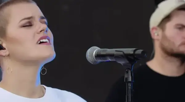 Taya Smith singt mit geschlossenen Augen und In-Ear-Monitoring. Ein Mann mit Kappe steht im Hintergrund.