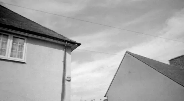 A black and white shot of two houses, captured on Kentmere 400 film. The image shows the roofs and walls of two buildings against a cloudy sky.