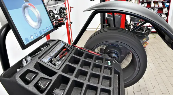 Reifen auf einer Wuchtmaschine mit Bildschirm und Werkzeugablage.