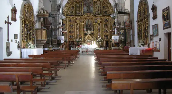 Interior de una iglesia con bancos de madera y un retablo dorado. Una pequeña maqueta de barco cuelga del techo, quizás en honor a la virxe da barca.