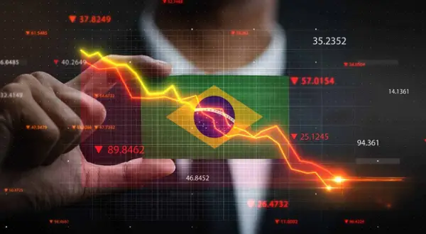 Ręka trzyma flagę Brazylii na tle wykresu finansowego. Kiedyś waluta Brazylii, real, doświadcza spadków.
