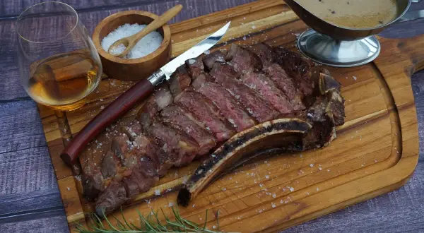 Ein saftiges Cote de Boeuf, perfekt geschnitten, mit grobem Salz bestreut, daneben ein Glas Whiskey, ein Messer und eine Sauce.