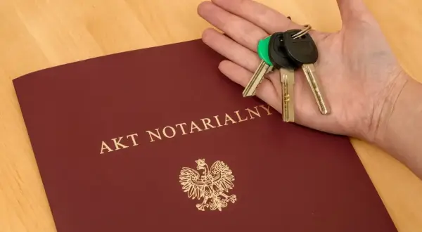 Akt notarialny i klucze w dłoni. Komparycja dokumentów i symbolu własności.