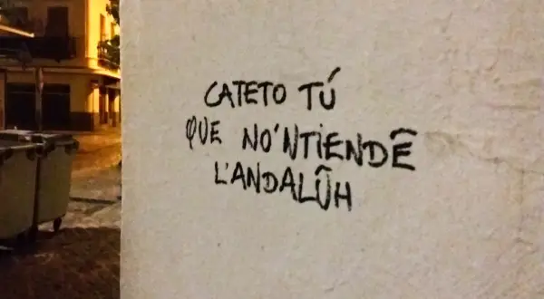 Graffiti en una pared con **expresiones sevillanas**: "Cateto tú que no'ntiende l'andalúh".