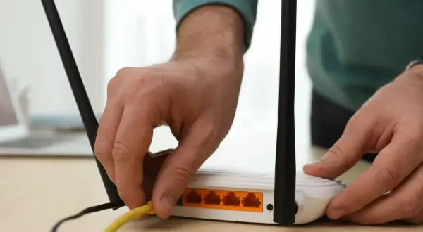 Ręka podłącza żółty kabel do routera. Dowiedz się, jak wzmocnić sygnał wifi domowym sposobem, by cieszyć się lepszym zasięgiem.