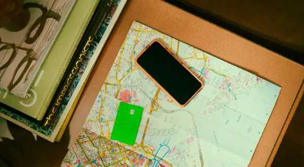 Zielona karta płatnicza, telefon i mapa leżą obok książek. Może to być przygotowanie do podróży, gdzie przyda się waluta Rumunii.