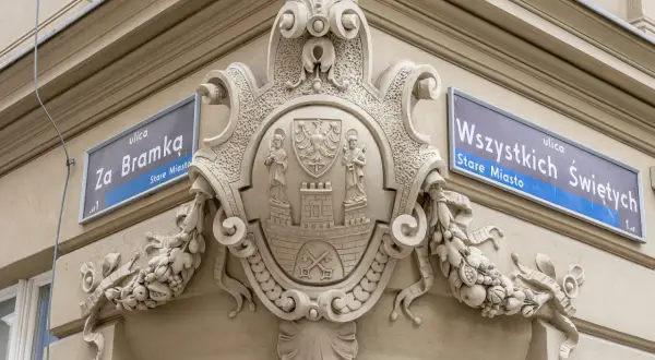 Bogaty herb zdobi fasadę kamienicy, obok tabliczek z nazwami ulic "Za Bramką" i "Wszystkich Świętych".