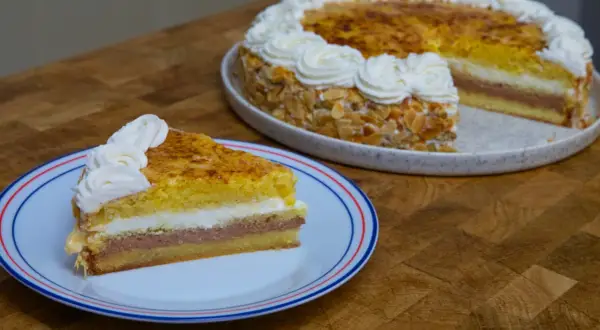 Un trozo de tarta o pastel de capas con crema y almendras, coronado con nata montada.