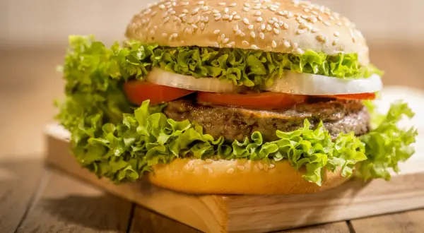 Soczysty burger z wołowiny, sałatą, pomidorem i cebulą w bułce do hamburgerów z sezamem. Idealny pomysł, co zrobić z bułki do hamburgerów.