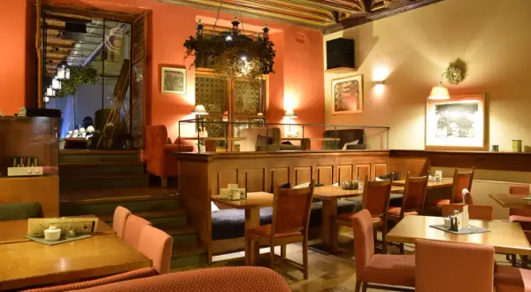 Przytulne wnętrze restauracji, gdzie zjeść w Krakowie na Rynku. Drewniane stoły, czerwone obicia i ciepłe oświetlenie tworzą atmosferę.
