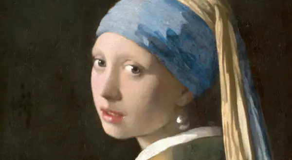 Dziewczyna z perłą, w błękitnym turbanie i złotej chuście, spogląda tajemniczo. Jej spojrzenie przyciąga uwagę.
