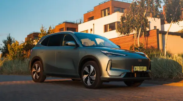 Nowy Geely EX5 w kolorze zielonym, zaparkowany przed nowoczesnymi domami.
