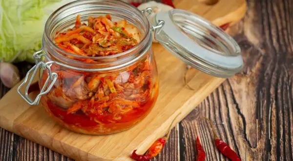 Słoik z domowym kimchi, idealny do przepisów na przetwory domowe. Obok kapusta, czosnek i papryczki chili.