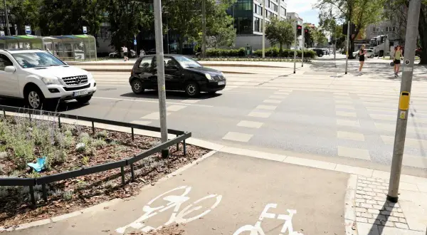 Czarny samochód wyprzedza na pasach, omijając białe auto. Na ścieżce rowerowej widoczne są symbole rowerów.