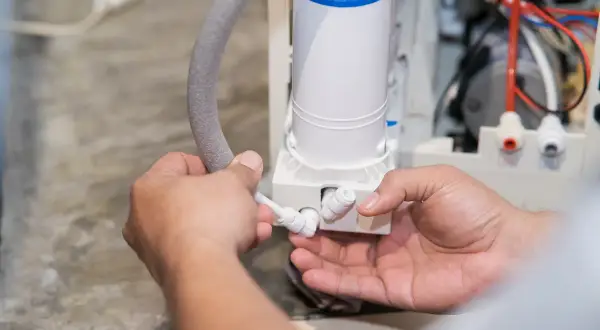 Mains d'un technicien connectant un tuyau à un adoucisseur d'eau, peut-être pour résoudre un problème d'eau salée.