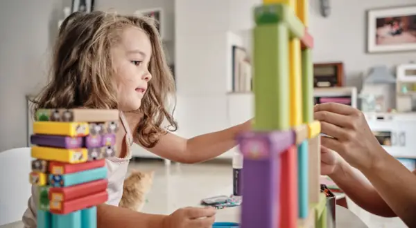 Niña concentrada construyendo con bloques de colores, disfrutando de juegos de habilidad para niños.