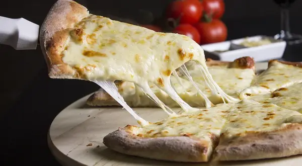 Kawałek pizzy z ciągnącym się serem, podniesiony łopatką.