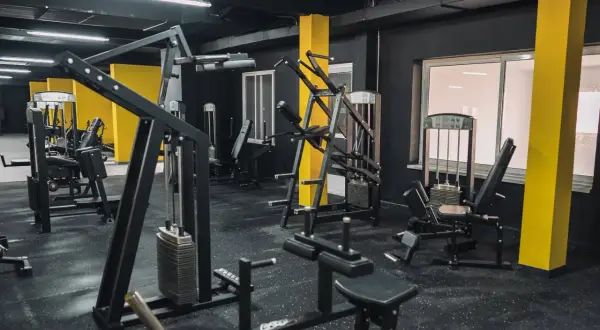 Gym med svarta väggar och gula pelare. Flera träningsmaskiner, inklusive en pec deck, står redo för ett träningspass.