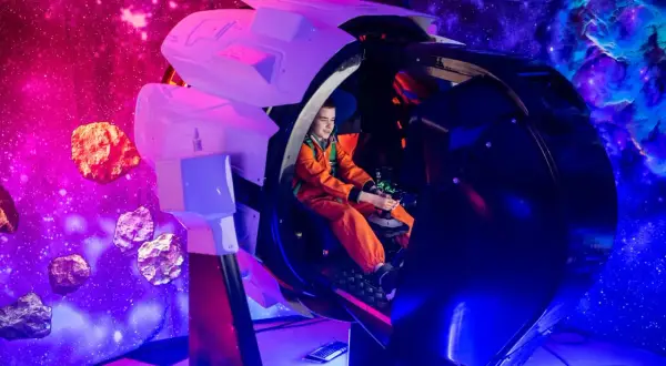 Chłopiec w pomarańczowym kombinezonie steruje statkiem kosmicznym w symulatorze. Kosmopark Wrocław oferuje kosmiczne przygody wśród asteroid i mgławic.
