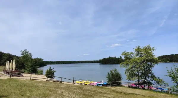 Słoneczny dzień nad jeziorem Chechło. Kolorowe rowerki wodne czekają na plaży, a w oddali widać zalesione brzegi.