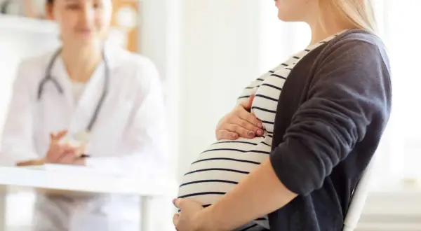 Schwangere Frau im Gespräch mit Ärztin, die den Bauch berührt. Möglicherweise geht es um einen kleinen zuckertest schwangerschaft.