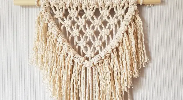 Un joli macramé tuto, suspendu à une tige de bois, avec des franges douces et un motif en losanges.