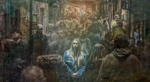 Młoda kobieta w dżinsowej kurtce stoi pośród tłumu, jej wyraz twarzy zdradza strach.