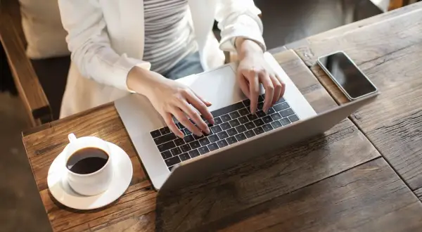 Kobieta pracuje na laptopie, realizując nest bank sesje przychodzące. Obok kawa i telefon.
