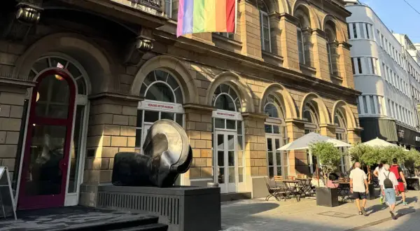 Ein Regenbogenbanner weht über dem von der Heydt Museum. Eine Skulptur steht davor, daneben ein Café mit Sonnenschirmen.