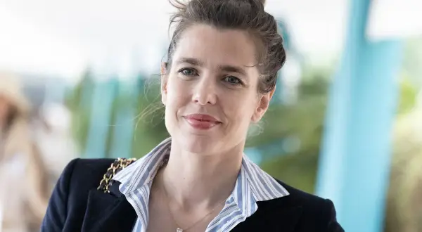 Carlota Casiraghi sonríe con su cabello recogido en un moño, luciendo un blazer oscuro y un collar con un colgante en forma de corazón.