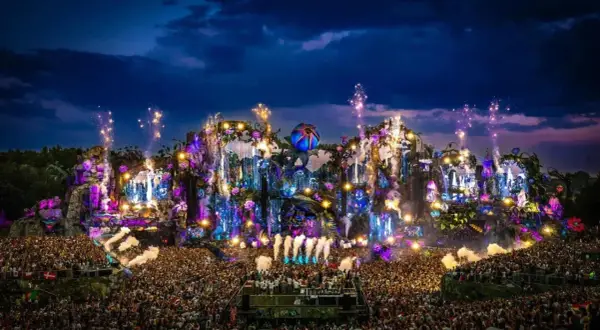 Un'enorme folla festeggia sotto un palco spettacolare, illuminato da luci colorate e fuochi d'artificio. È il luogo dove fanno il Tomorrowland, un'esplosione di musica e magia.