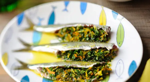 Trois sardines farcies aux herbes et légumes, servies sur une assiette décorée de poissons.