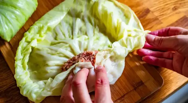 Ręce zwijają gołąbki z farszem mięsnym w liście kapusty. Idealny przepis na gołąbki na 1kg mięsa.