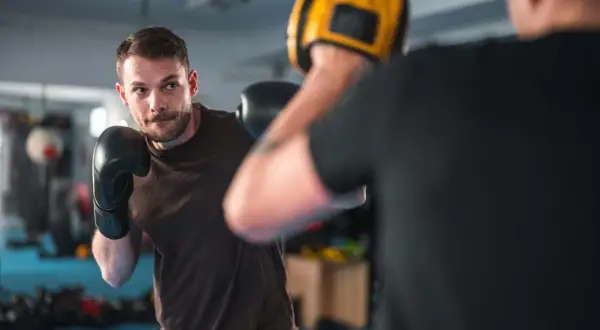 A man in black boxing gloves practices his boxing workout routine, focusing on his opponent holding a yellow mitt.