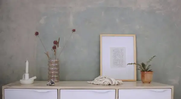 Un tavolino con candela, vaso di fiori secchi, quadro e corda. Sembra la preparazione calce per imbiancare, con un tocco artistico.