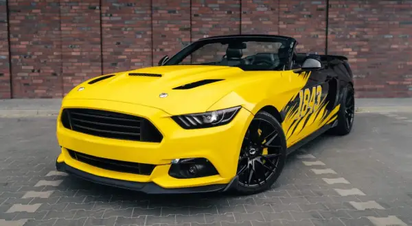 Żółty kabriolet Mustang z czarnymi akcentami i grafiką "1849" na boku. Wygląda jak model z 2026 roku, gotowy na podbój dróg.