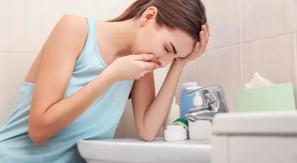 Gravid kvinna med illamående vid handfatet, hon håller handen för munnen. Kanske behöver hon medicin.