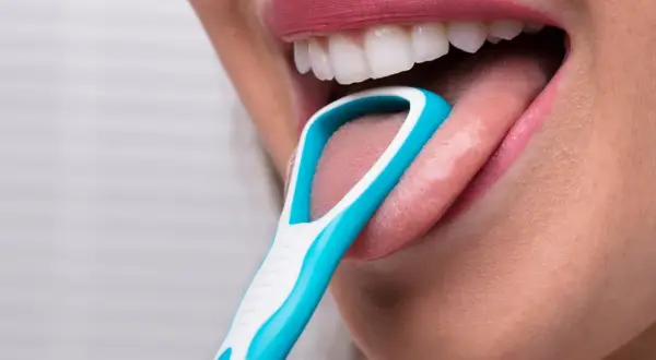 Una persona usa un puliscilingua azzurro per pulire la lingua, un gesto che ricorda la lava lingua.